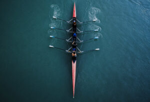 Kayak from above with 4 rowing people. Blue and aqua water background. Sport and moving concept. Red kayak and 8 paddles.